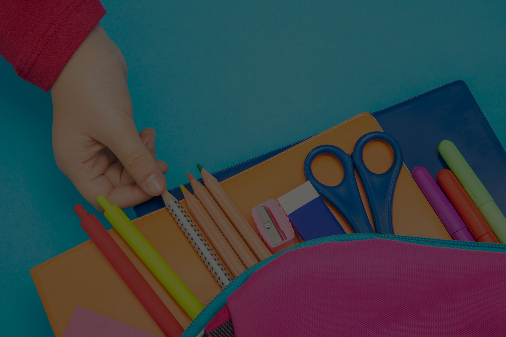 Child's hand reaching for pencil from binder of school supplies